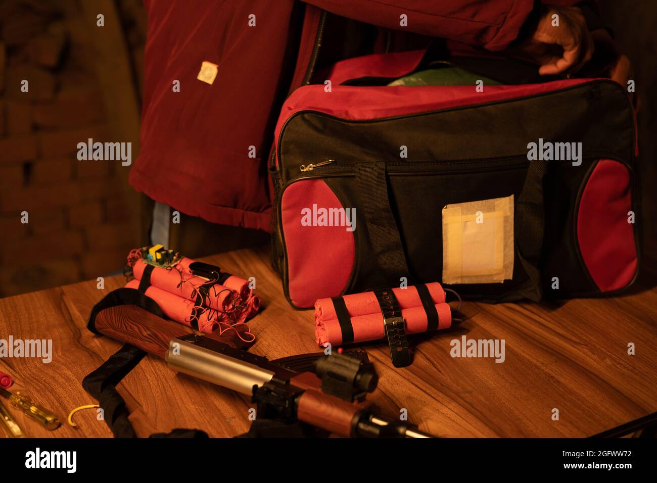 Focus on red dynamite, unrecognizable militent or soldier preparing by placing time bomb with dynamite and gun inside the bag Stock Photo