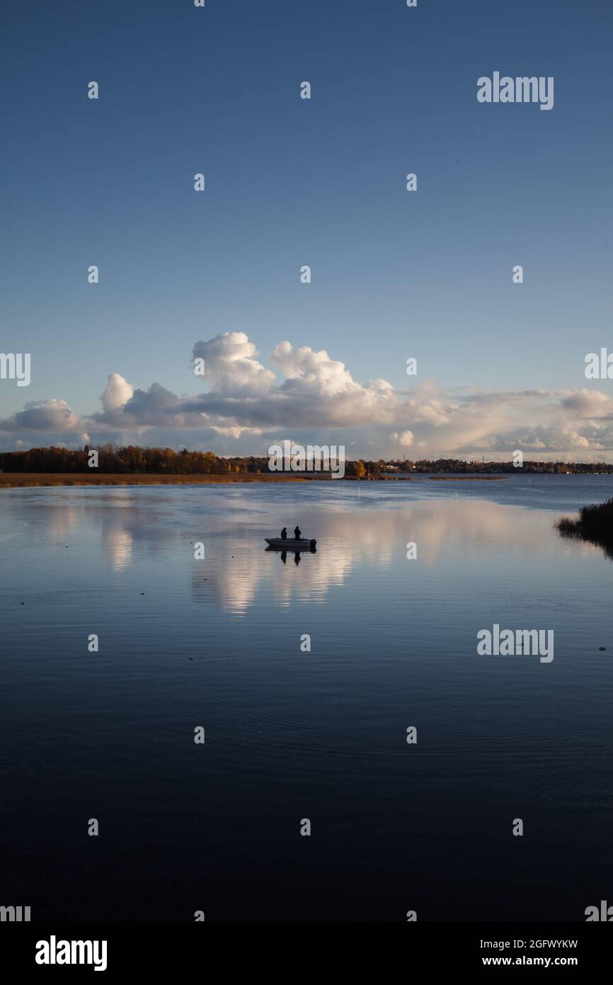 Seascape, calm sea with two fishermen on a boat and clouds reflecting on the blue water. Stock Photo