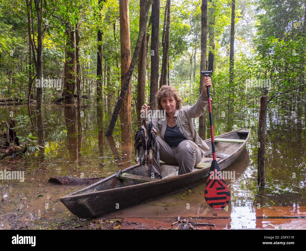 Caucasian woman in the small wooden boat with fishes catch from the lagoon in Amazon rainforest. Amazonia. Brazil. Latin America Stock Photo