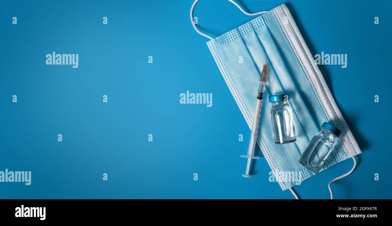 vaccination - vaccine vials with syringe and medical face mask on blue background. banner copy space Stock Photo