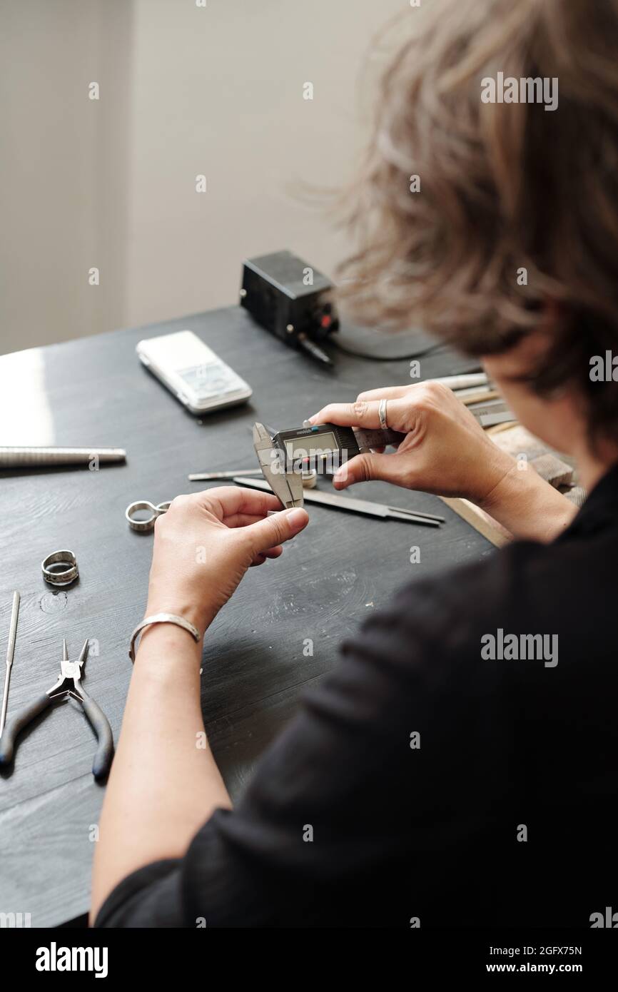 Over shoulder view of female jeweler measuring ring width using caliper in workshop Stock Photo