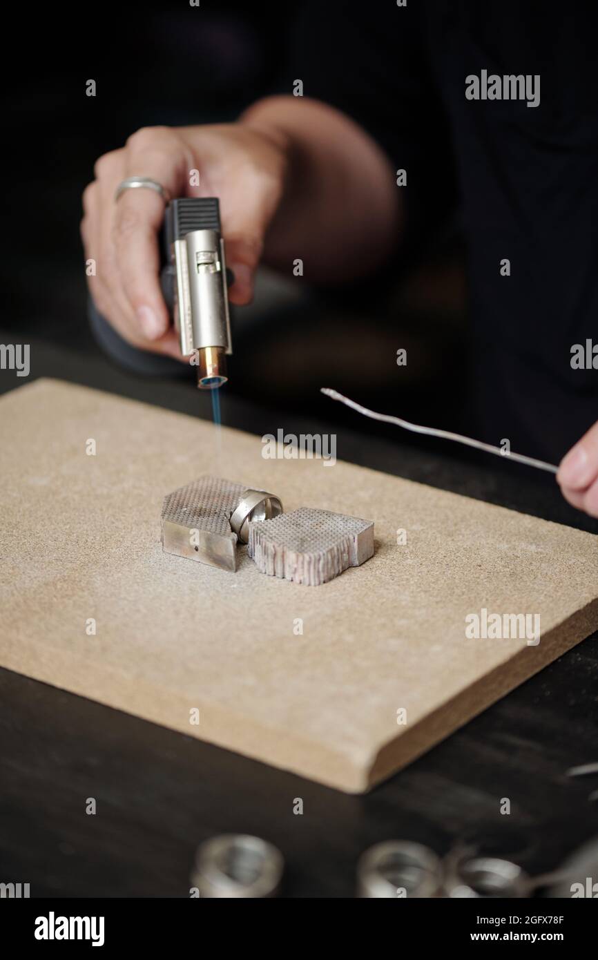 Hands of jeweler soldering silver ring with torch on board in workshop Stock Photo