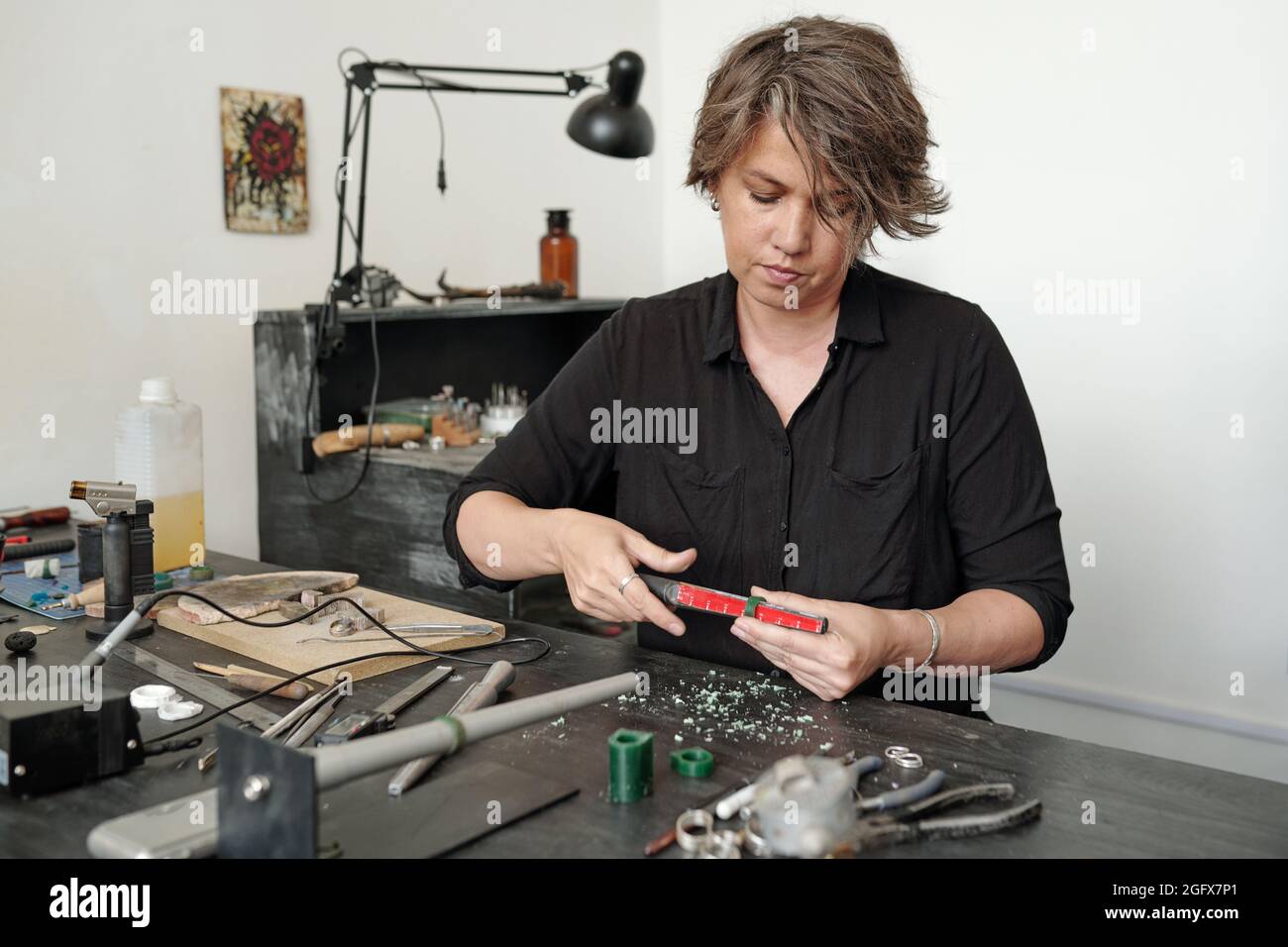 Concentrated middle-aged jeweler sitting at dirty desk and checking size of ring in workshop Stock Photo