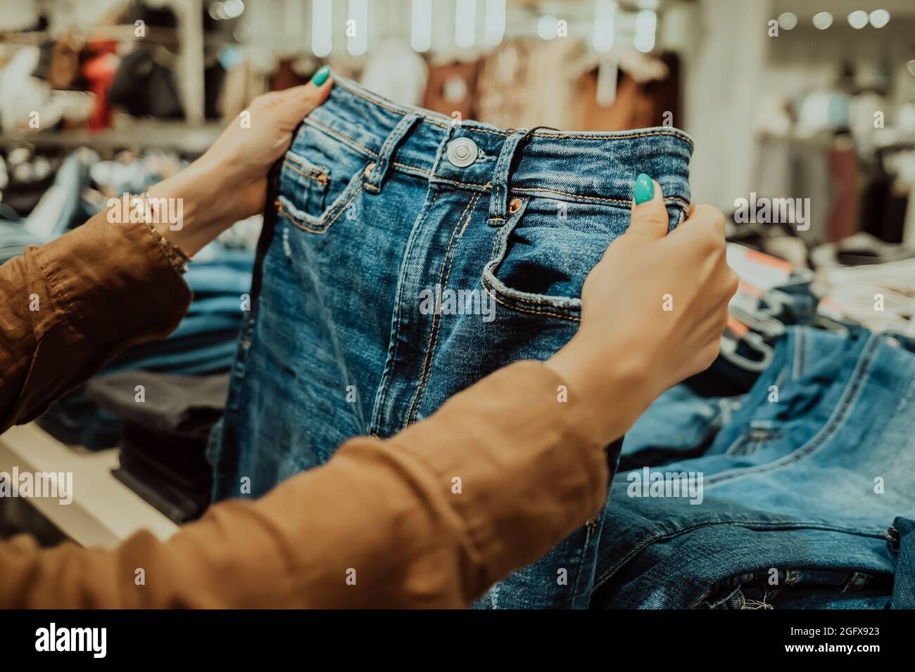 Young woman in fashion store chooses things for herself - jeans, denim trousers. Customers, shopping, sales concept. Stock Photo