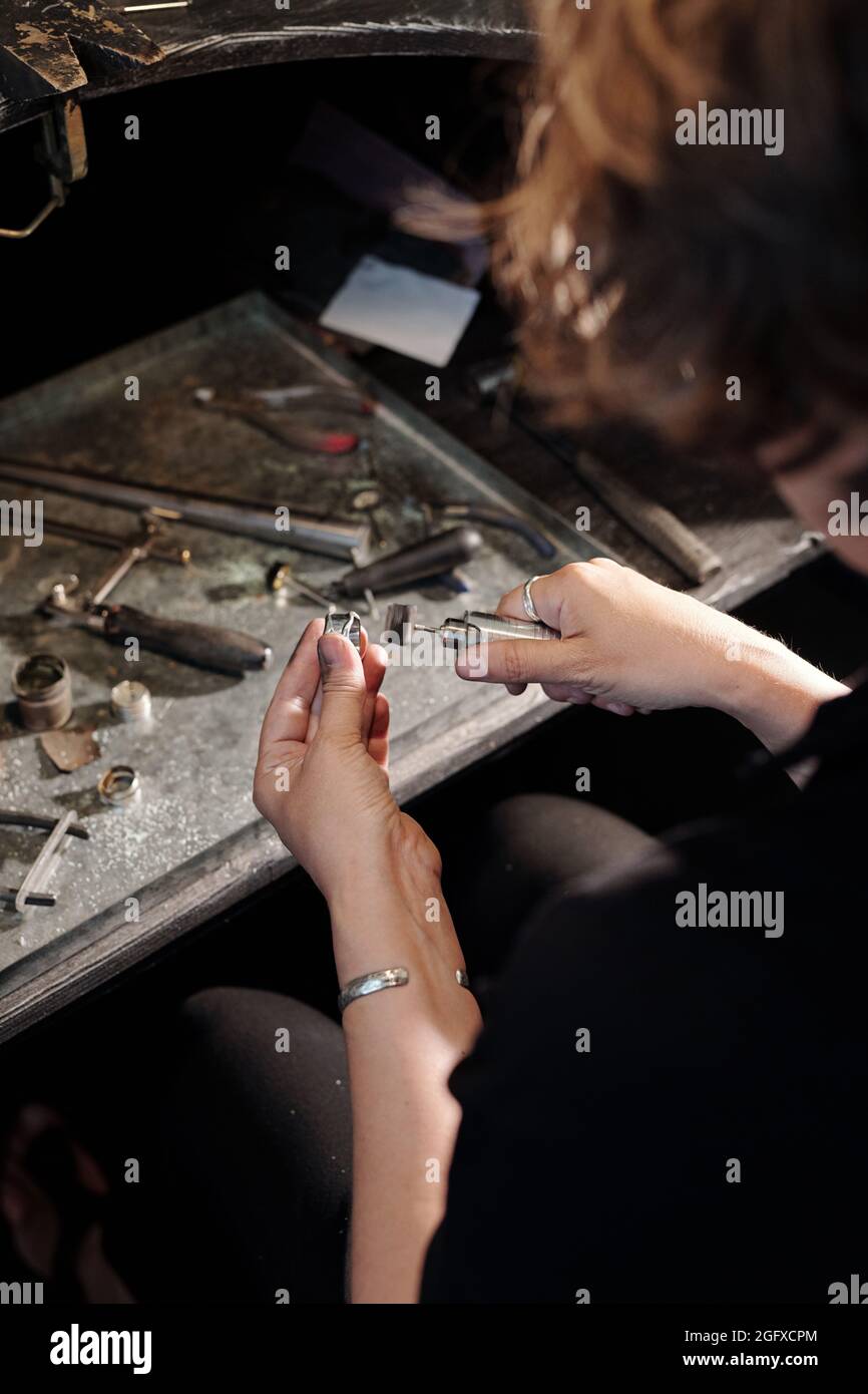 Over shoulder view of female bench jeweler using hand polisher while performing jewelry repair in workshop Stock Photo