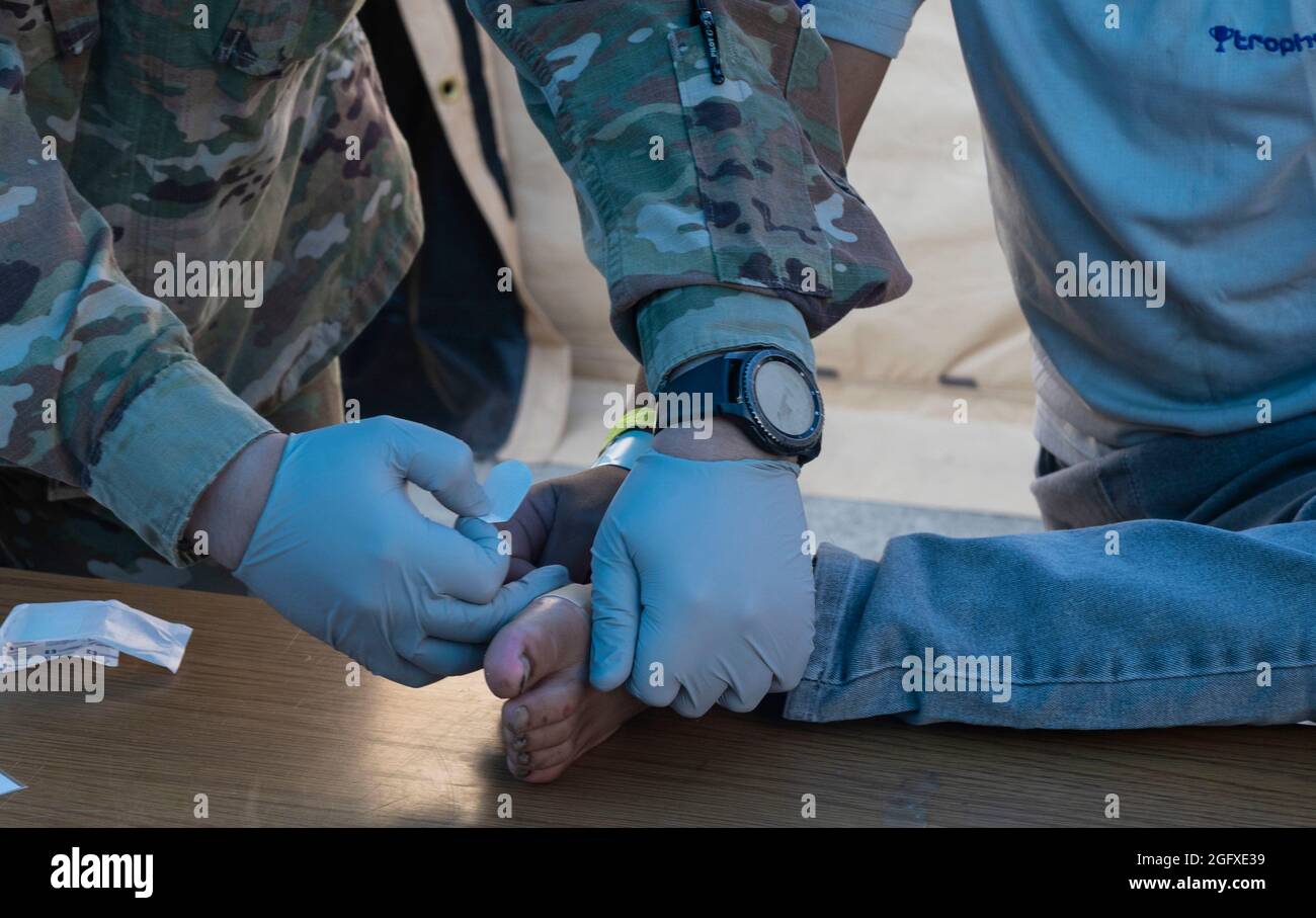 A U.S. Air Force Airman assigned to the 86th Airlift Wing Medical Group, places a band-aid on the foot of an evacuee during Operation Allies Refuge Aug. 25, 2021 at Ramstein Air Base, Germany. The 86th MDG is providing medical and dental support for evacuees until they can be transported to more permanent resettlement locations. Team Ramstein is providing safe, temporary lodging for evacuees from Afghanistan. Operation Allies Refuge is facilitating the quick, safe evacuation of U.S. citizens, Special Immigrant Visa applicants, and other at-risk Afghans from Afghanistan. (U.S. Air Force photo b Stock Photo