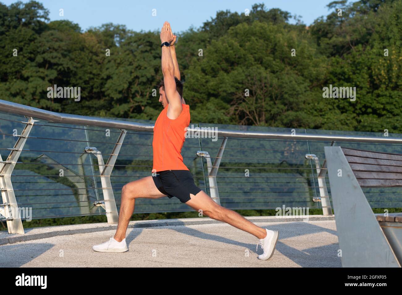 Feel the stretch in your hip. Man do crescent lunge stretch raising arms. Doing yoga or pilates exercise Stock Photo