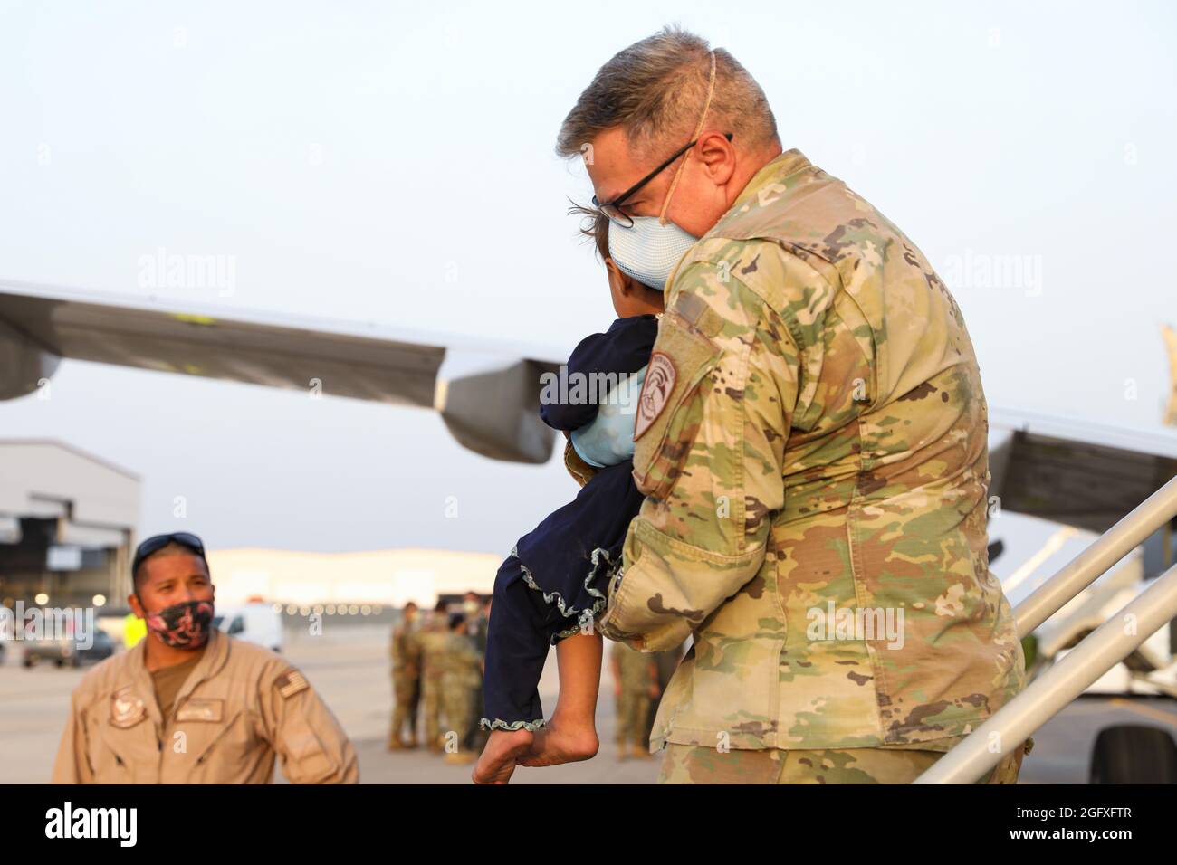 NAVAL AIR STATION SIGONELLA, Italy (Aug. 26, 2021) – A U.S. Service member helps an Afghanistan evacuee depart a U.S. Air Force C-40B Clipper at Naval Air Station Sigonella Aug. 26, 2021. NAS Sigonella is currently supporting the Department of Defense mission to facilitate the safe departure and relocation of U.S. citizens, Special Immigration Visa recipients, and vulnerable Afghan populations from Afghanistan. NAS Sigonella’s strategic location enables U.S, allied, and partner nation forces to deploy and respond as required to ensure security and stability in Europe, Africa, and Central Comma Stock Photo