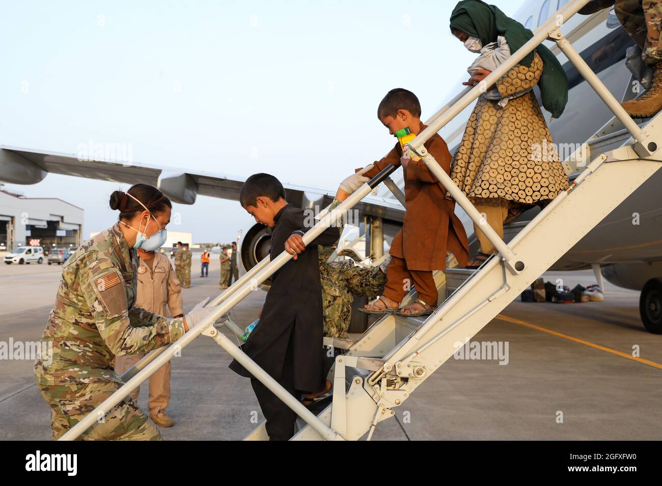 NAVAL AIR STATION SIGONELLA, Italy (Aug. 26, 2021) – U.S. Service members help Afghanistan evacuees depart a U.S. Air Force C-40B Clipper at Naval Air Station Sigonella Aug. 26, 2021. NAS Sigonella is currently supporting the Department of Defense mission to facilitate the safe departure and relocation of U.S. citizens, Special Immigration Visa recipients, and vulnerable Afghan populations from Afghanistan. NAS Sigonella’s strategic location enables U.S, allied, and partner nation forces to deploy and respond as required to ensure security and stability in Europe, Africa, and Central Command. Stock Photo