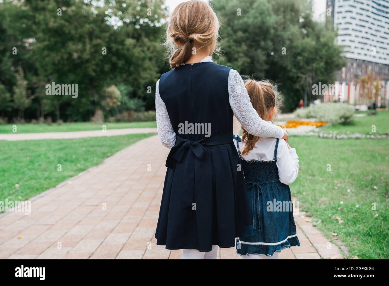 Back to elementary school concept. Little girl in school uniform goes to first grade with little sister on first of September. Ceremony of graduating. Stock Photo