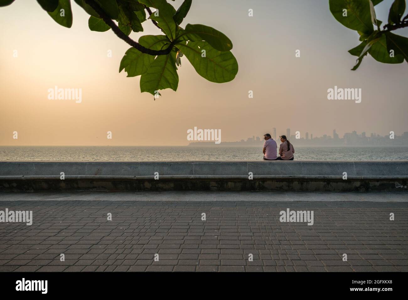 Mumbai, Maharashtra, India - 20 Nov 2019: A couple sitting and enjoying the sea view in the late evening with the sun setting at Nariman Point in Mumb Stock Photo