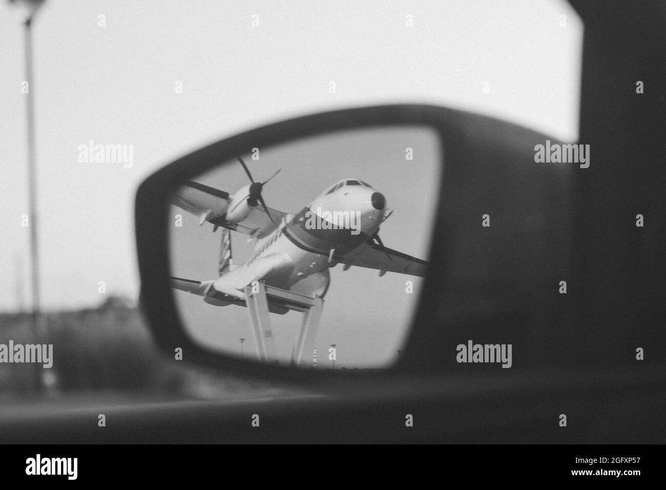 Black and white shot of an aircraft reflection to the mirror of a car Stock Photo
