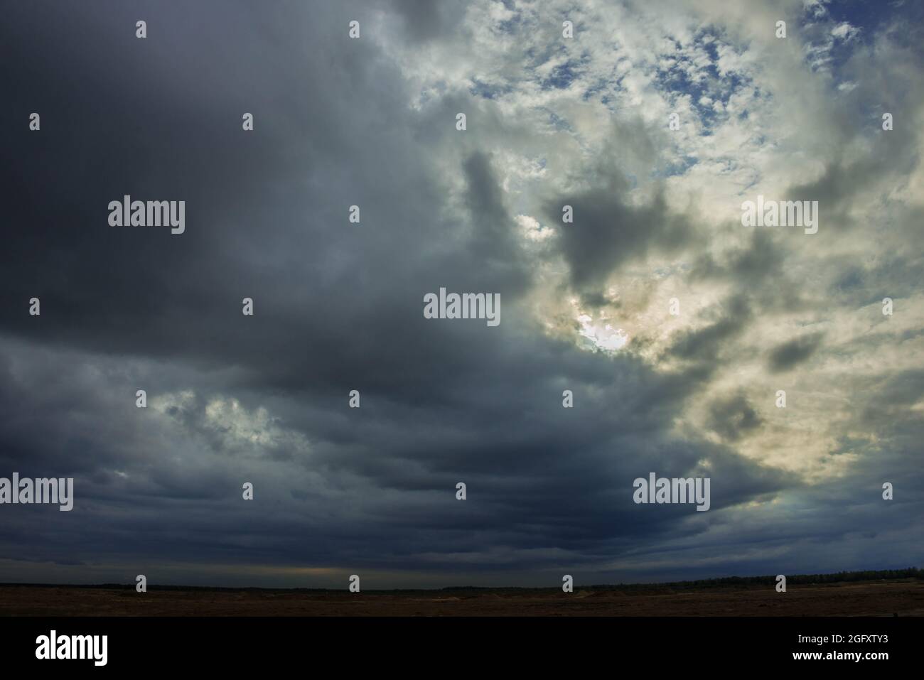 A vast plain covered with arable fields and meadows. The sky is overcast, covered with dark, awe-inspiring clouds that herald the impending downpour. Stock Photo