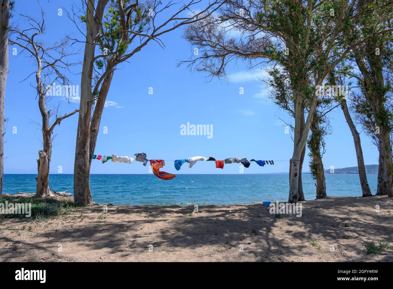 Campers clothes drying on a washing line, strung between trees, next to the sea on a beach in Southern Greece. Stock Photo