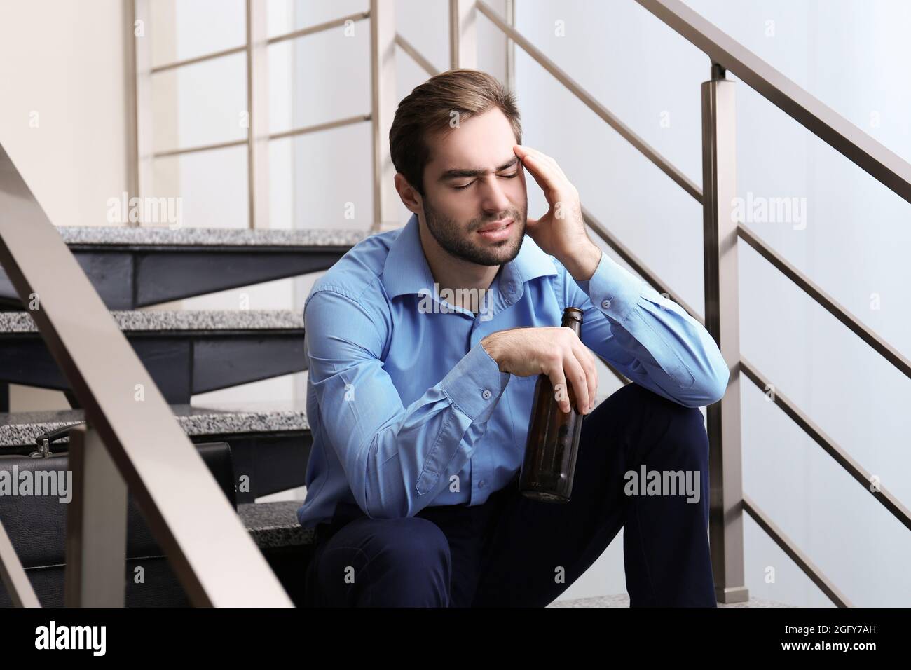 Tired office worker sitting on stairs with bottle of beer Stock Photo ...