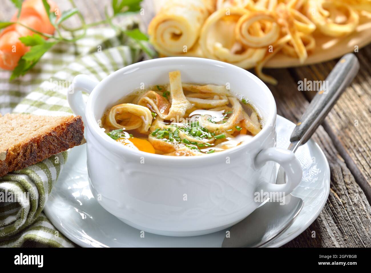 Delicious homemade beef broth with pancake strips, served with bread on a wooden table Stock Photo
