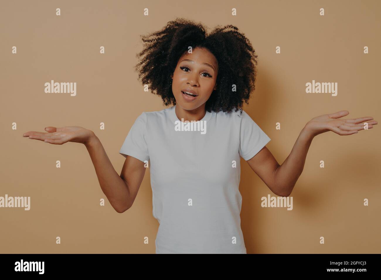 Unsure african woman woman shrugging shoulders and spreading arms sideways, isolated over beige wall Stock Photo