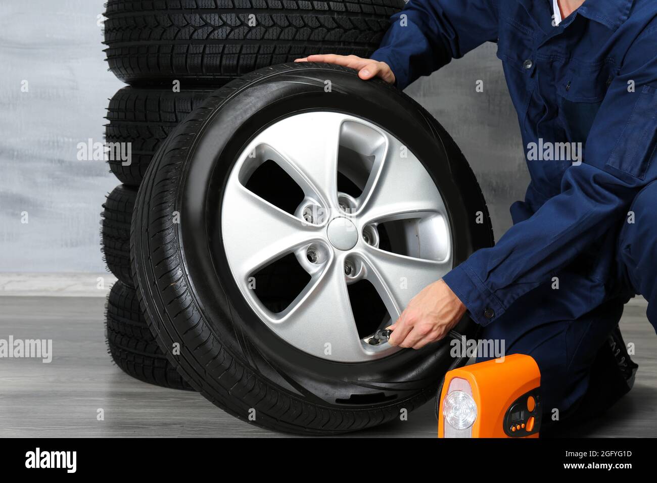 Young mechanic in uniform with wheels, on gray background Stock Photo