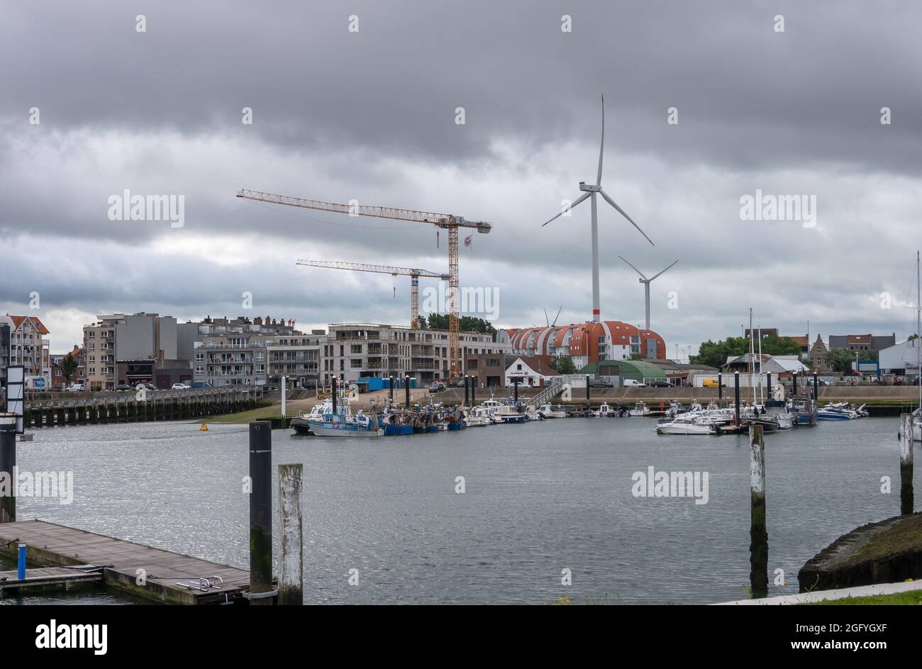 Zeebrugge Port, Belgium - August 6, 2021: Werfkaai section of yacht harbor with tall windmills and construction cranes in back under heavy rainy cloud Stock Photo