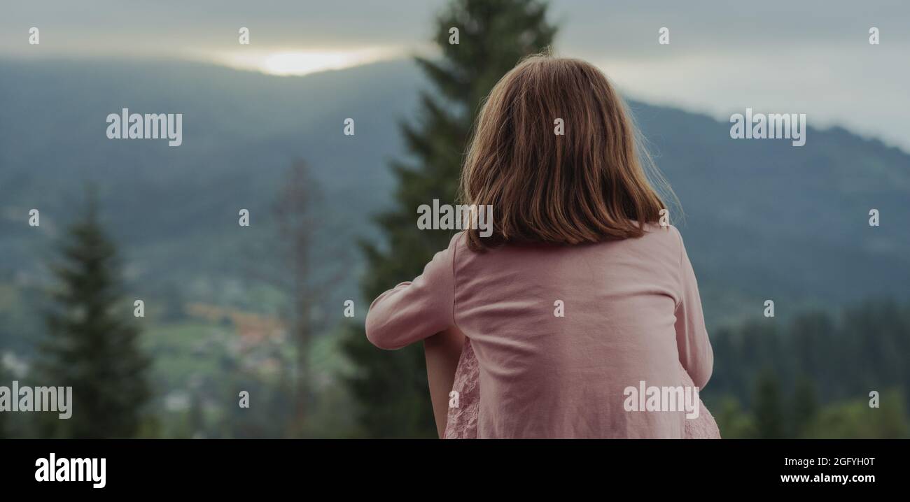 Panoramic shot of a little girl watching sunset in the mountains Stock Photo