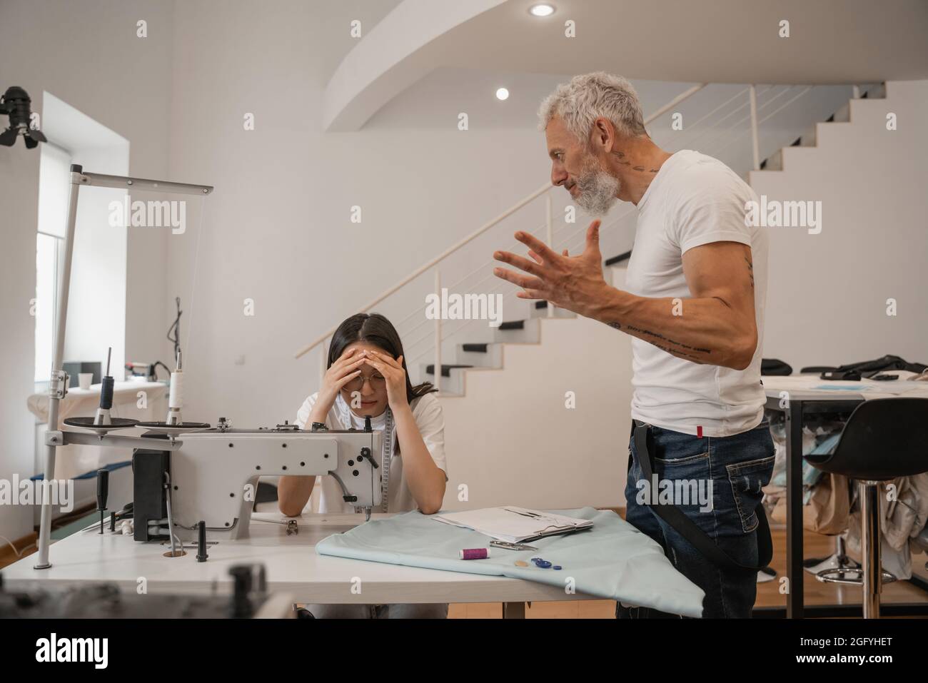 Angry designer standing near scared asian colleague in atelier Stock ...