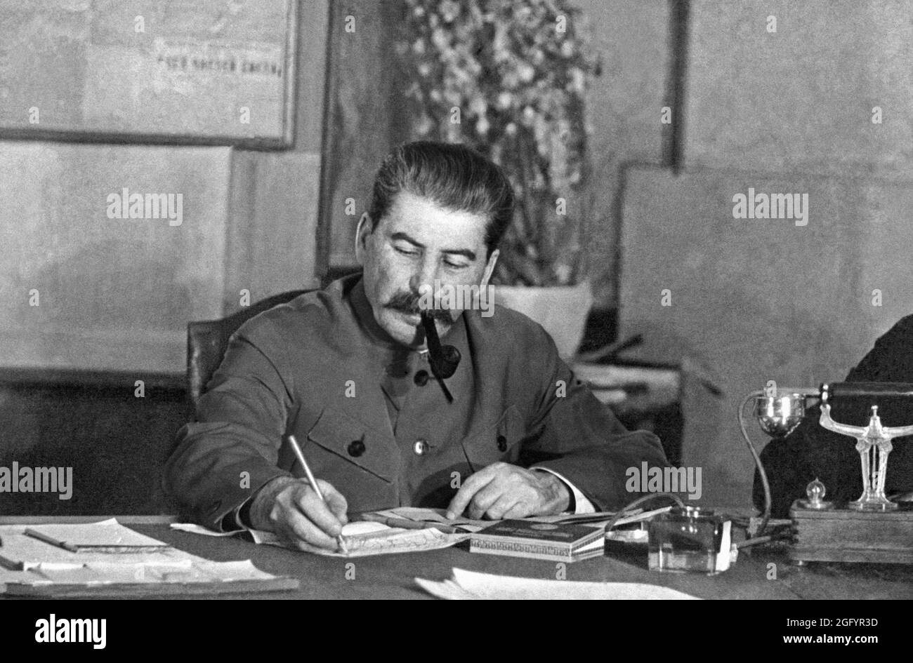 Joseph Stalin, with his pipe, writing at a desk at a conference in the Kremlin, Moscow, March 1935. He is writing with his trademark coloured pencil with which he wrote everything. Stock Photo