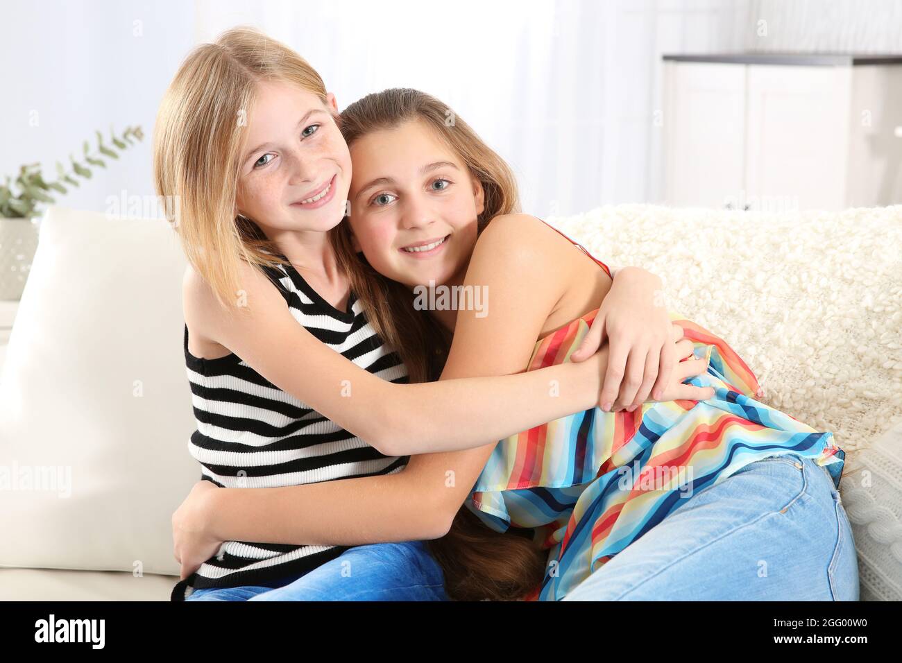 Two cute girls sitting on sofa Stock Photo - Alamy