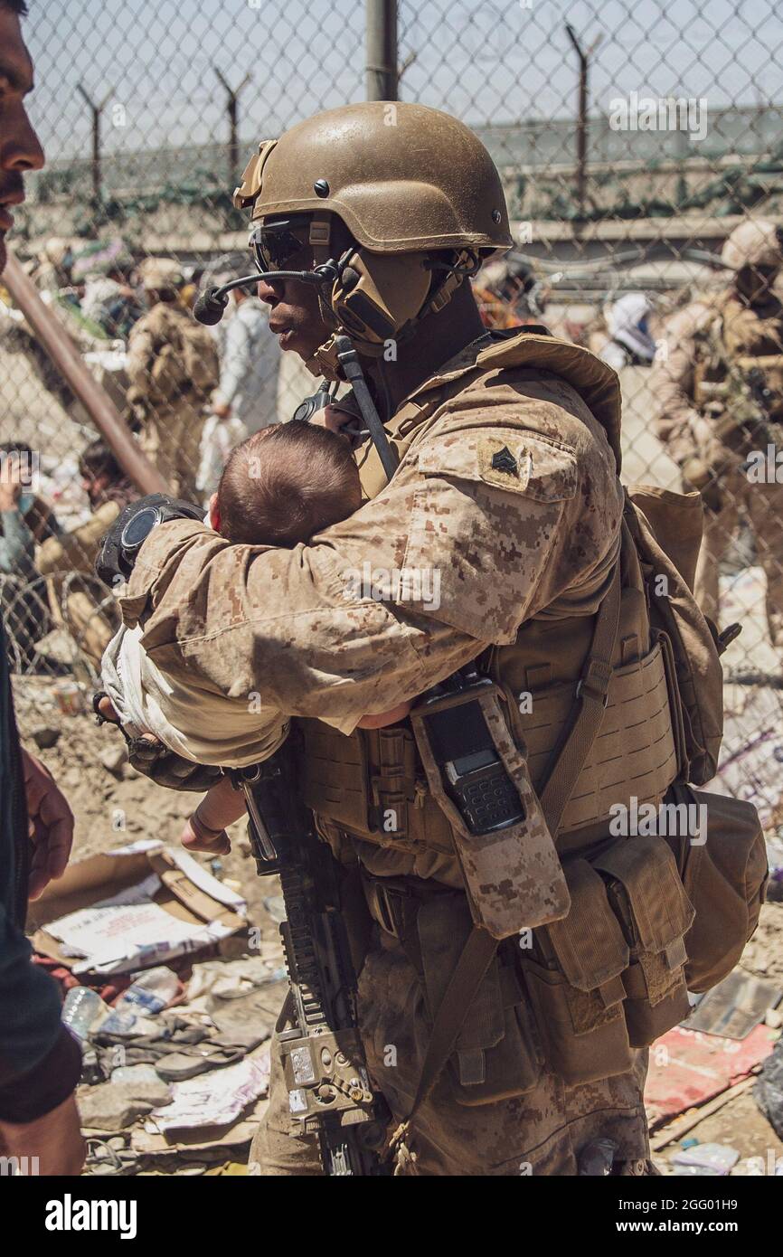 A U.S. Marine with Special Purpose Marine Air-Ground Task Force - Crisis Response - Central Command takes care of baby that is processing at an Evacuation Control Checkpoint (ECC) during an evacuation at Hamid Karzai International Airport, Kabul, Afghanistan, Aug. 26. U.S. service members are assisting the Department of State with a non-combatant evacuation operation (NEO) in Afghanistan. (U.S. Marine Corps photo by Staff Sgt. Victor Mancilla) Stock Photo