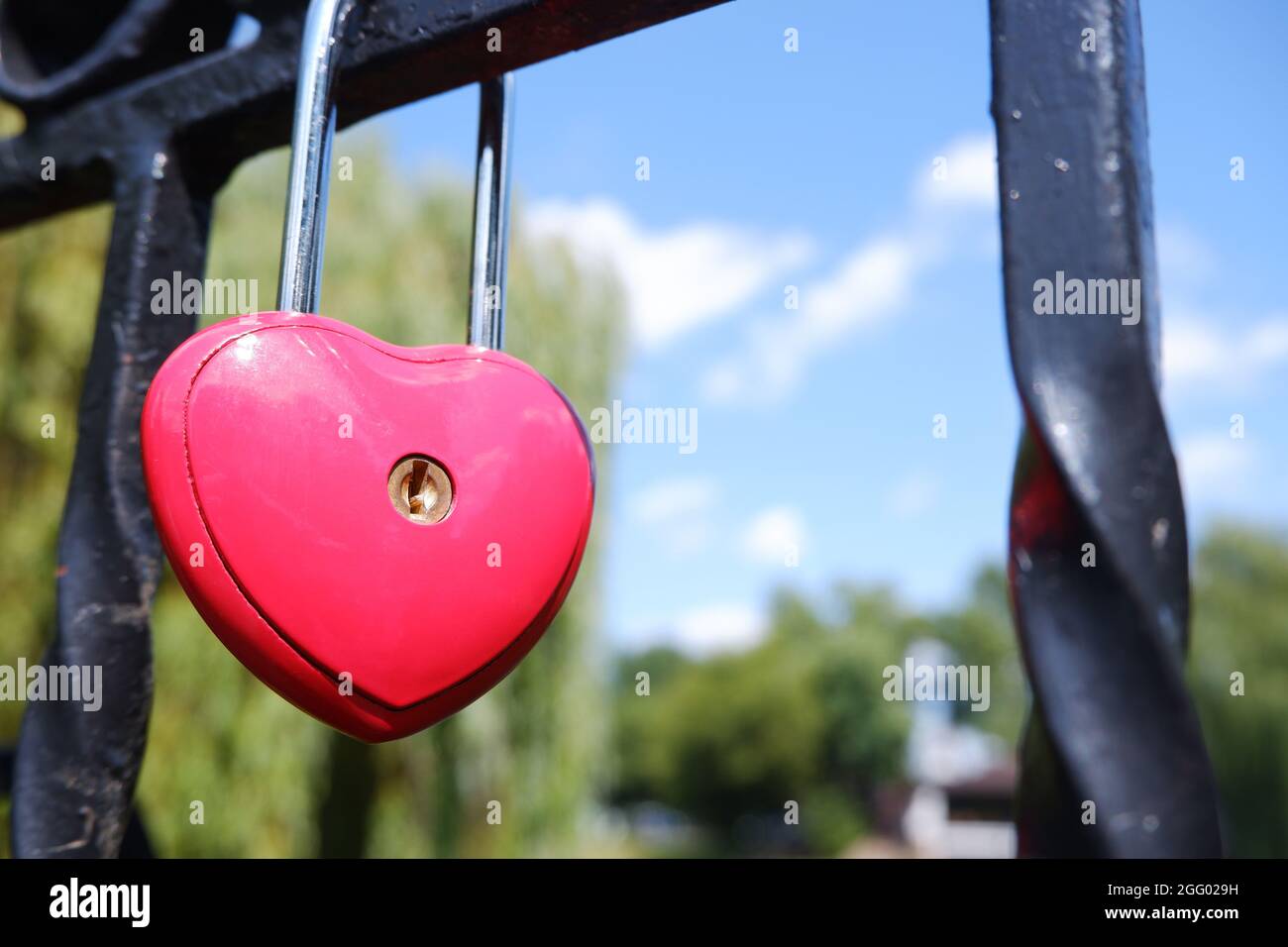 Metal red door lock in the shape of a heart on the fence as a symbol of ...