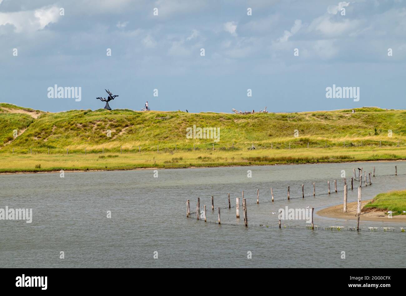 Knokke-Heist, Flanders, Belgium - August 6, 2021: Zwin Nature Reserve. Black Keun statue on green dunes separating salt marsh creek from Nord Sea unde Stock Photo