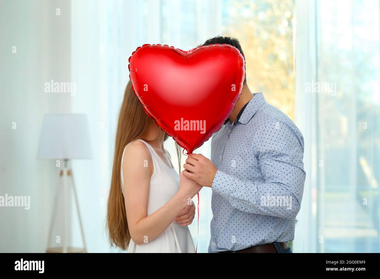 Cute young couple with red balloon in shape of heart at home Stock ...