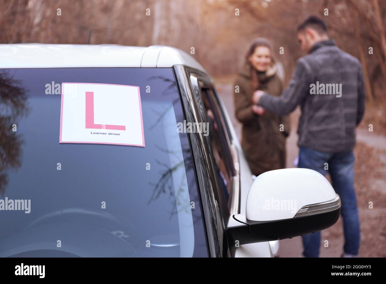 Driver Instructed Car Sign Learner driver sign on car windscreen. Blurred view of instructor and ...