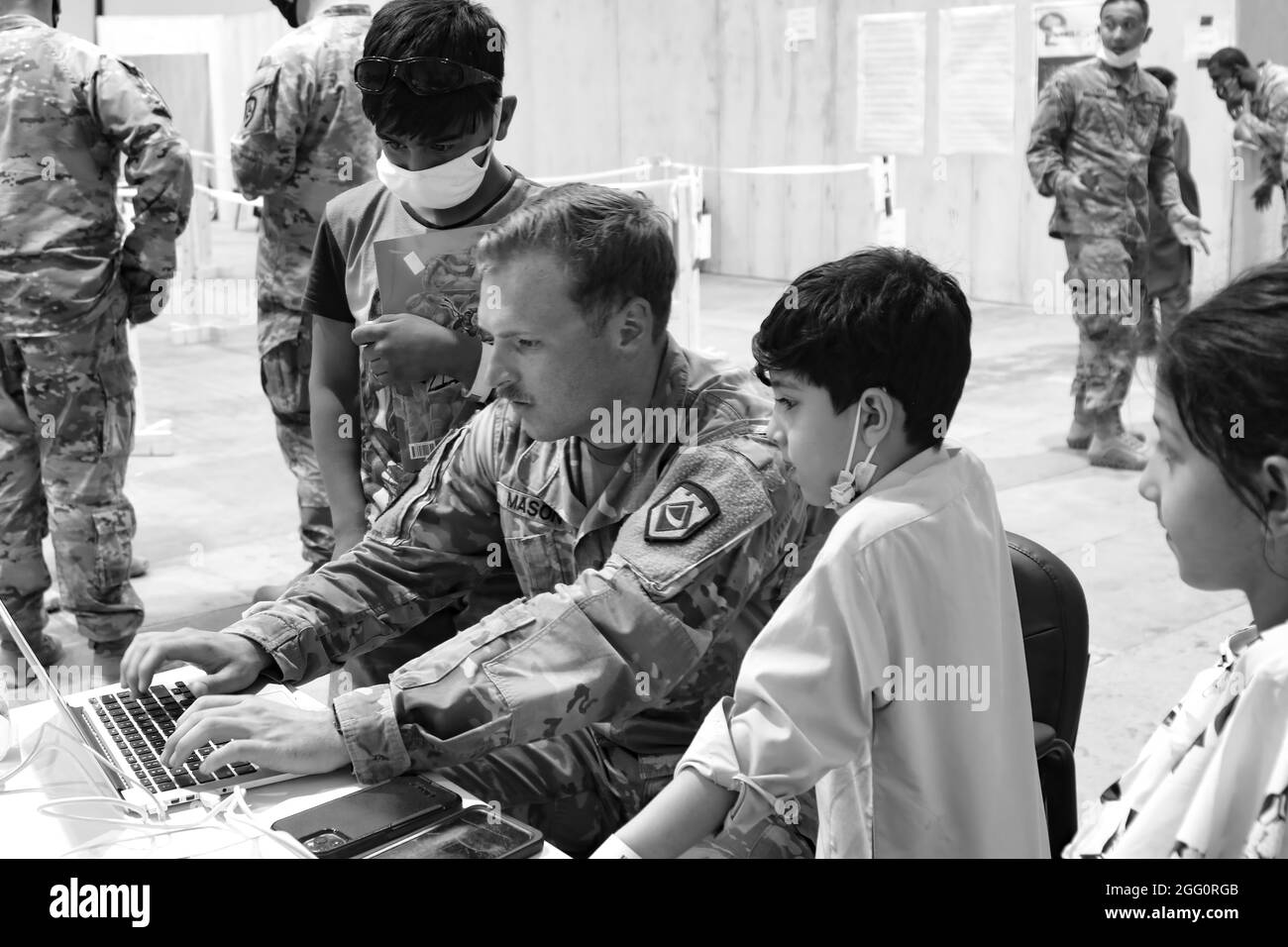 A U.S. Army National Guard Soldier with Task Force Spartan, U.S. Army Central shares his computer to entertain Afghan evacuee children at Camp Buehring, Kuwait, Aug. 25, 2021. USARCENT Soldiers hit it off quickly with the children at the facility, finding ways to bring smiles and entertain them through the arrival process. (U.S. Army photo by Pfc. Katelynn Bissell) Stock Photo