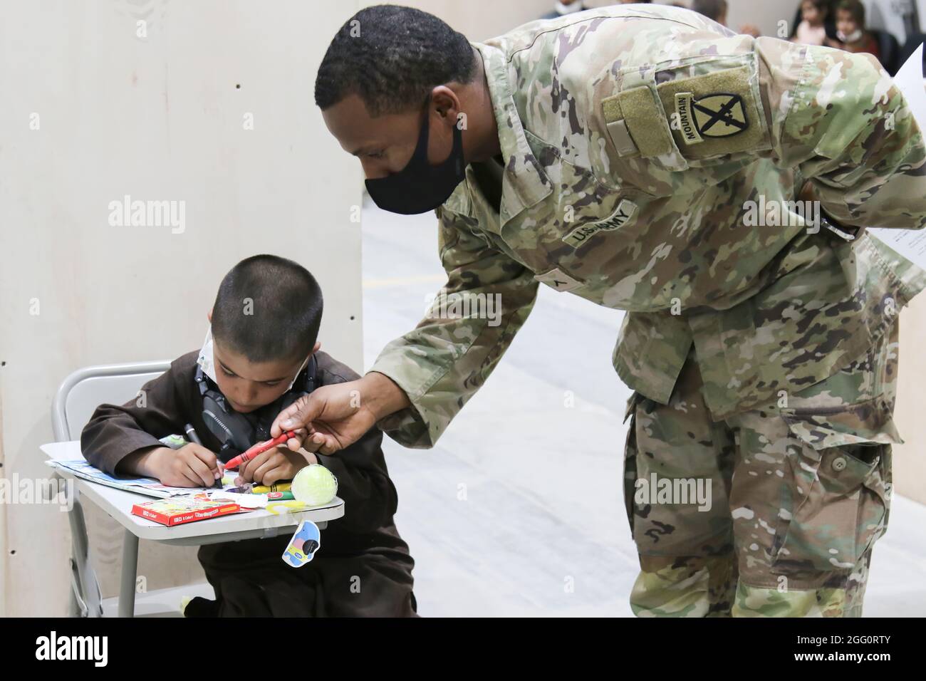 A U.S. Army Soldier and Afghan evacuee boy color together at Camp Buehring, Kuwait, Aug. 25, 2021. Soldiers joined in activities with the children as their families went through arrival processes at the facility. (U.S. Army photo by Sgt. Marc Loi) Stock Photo