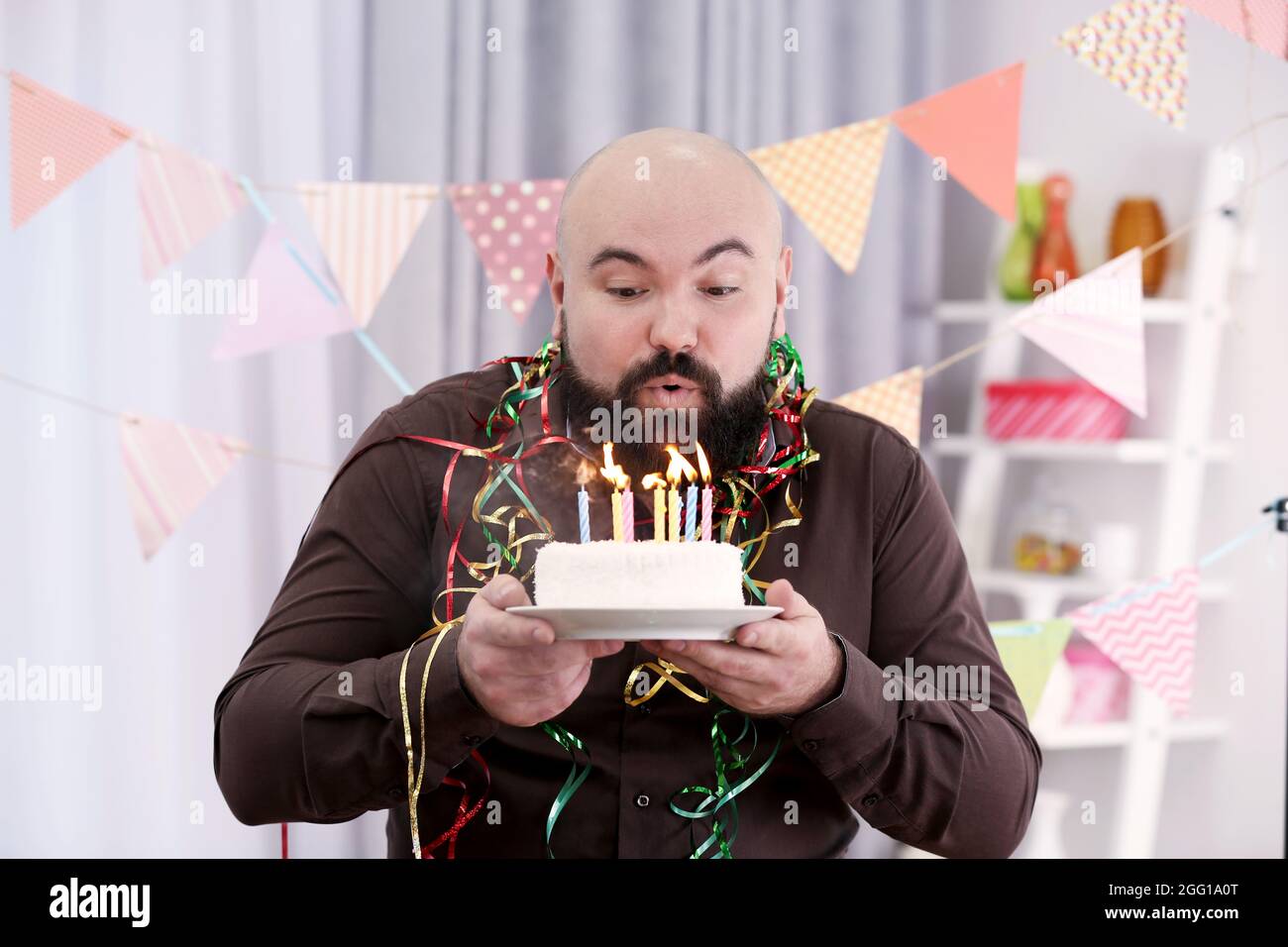 Funny fat man blowing out candles on birthday cake at party Stock Photo