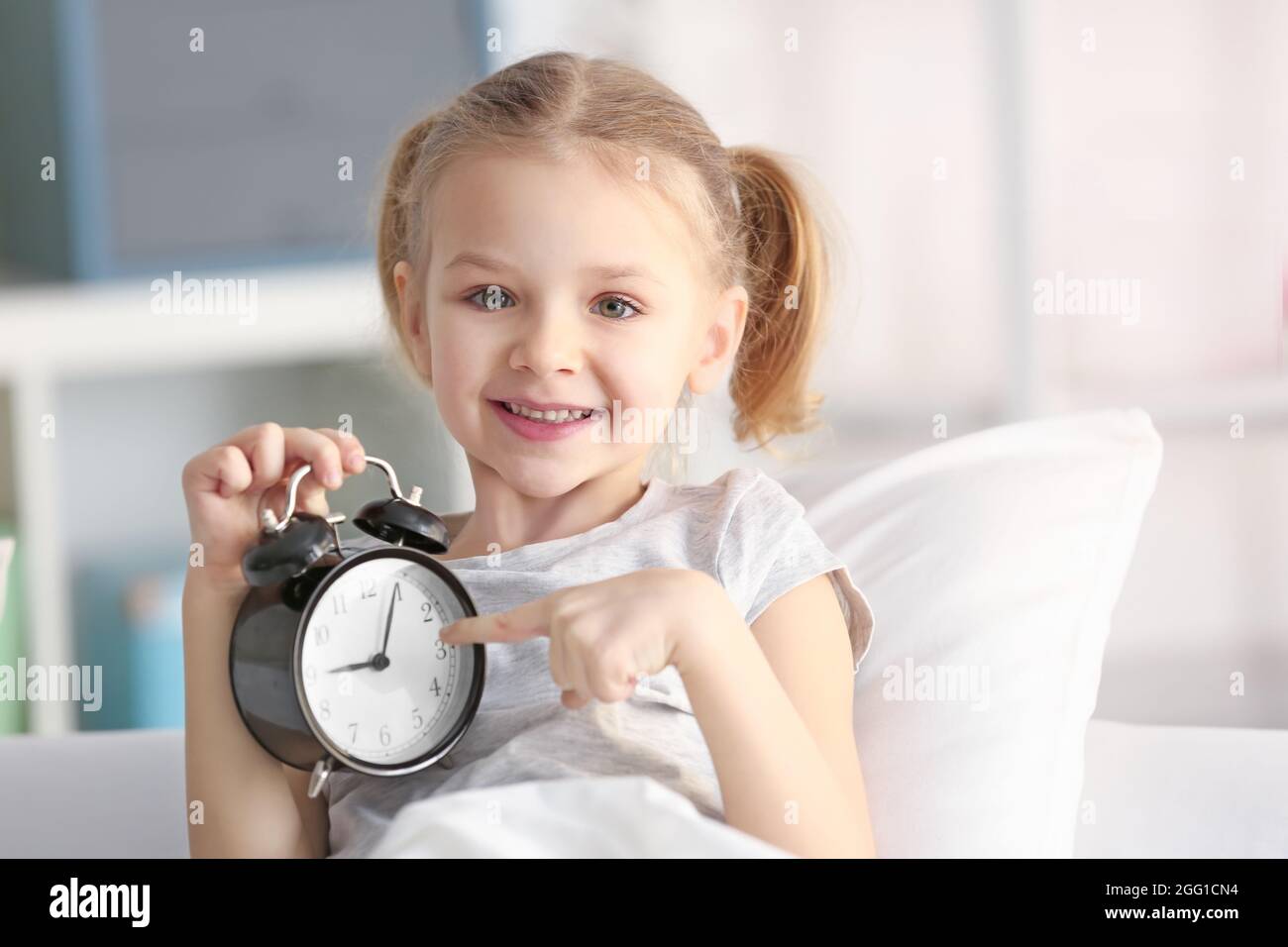 Cute little girl with alarm clock in bed Stock Photo Alamy
