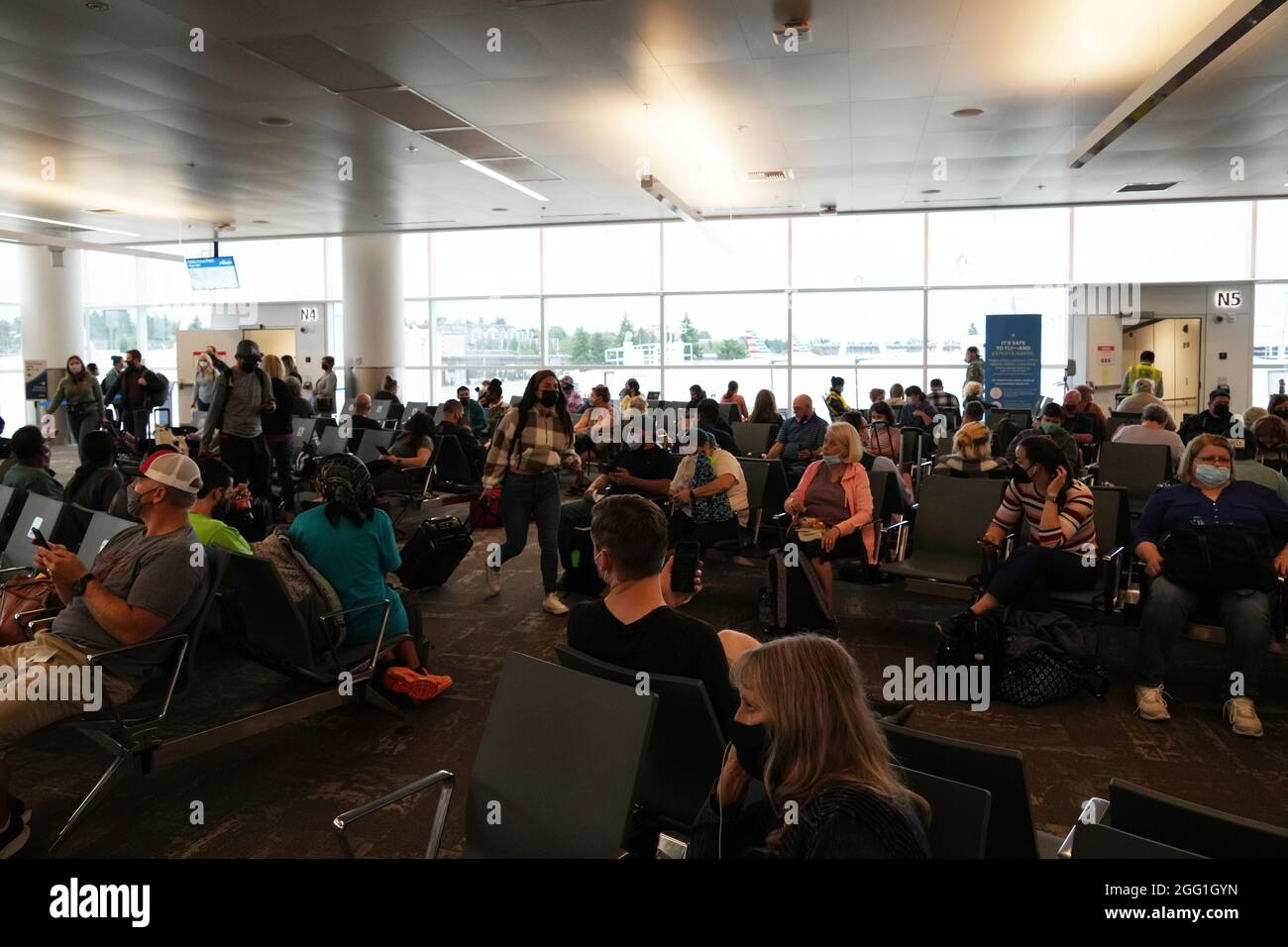 People with face masks sit in the waiting area of the N4 and N5 games at the North Terminal of the Seattle-Tacoma International Airport, Friday, Aug. Stock Photo