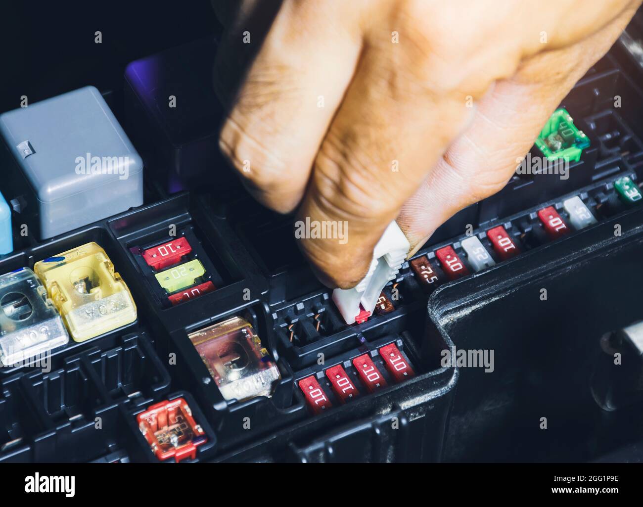 Mechanic replaces the spare fuse to the car fuse box with the fuse clip tool Stock Photo
