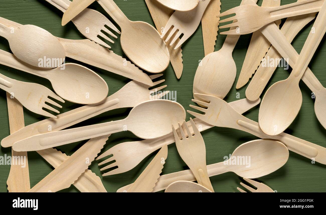 Disposable tableware from natural materials. Pile of wooden spoon, fork, knife on green wooden table Stock Photo