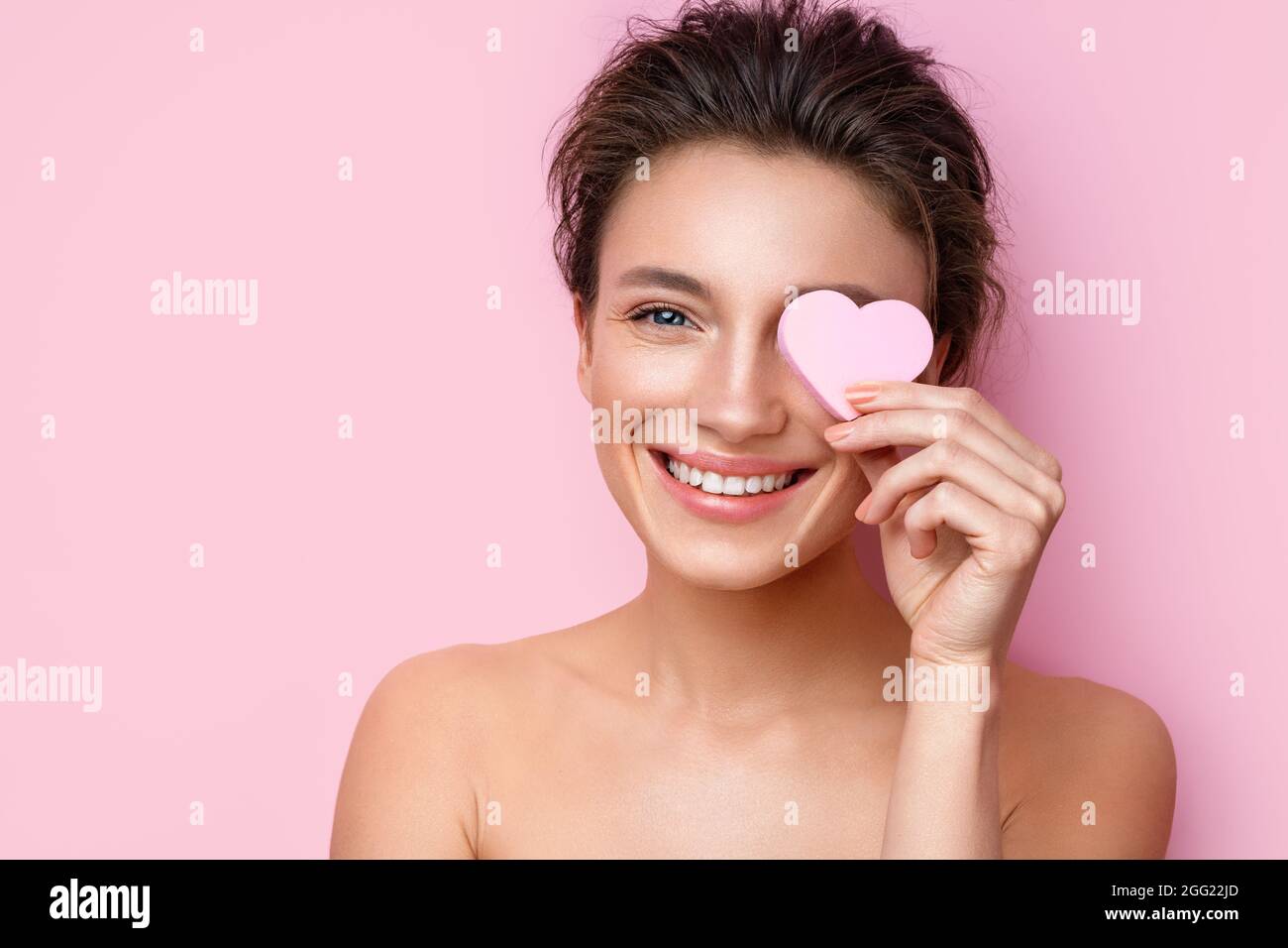 Smiling woman with cosmetic sponge covering one eye. Photo of woman with perfect makeup on pink background. Beauty concept Stock Photo