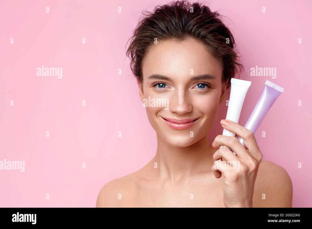 Smiling woman holds tubes with cosmetic cream. Photo of attractive woman with perfect makeup on pink background. Beauty concept Stock Photo