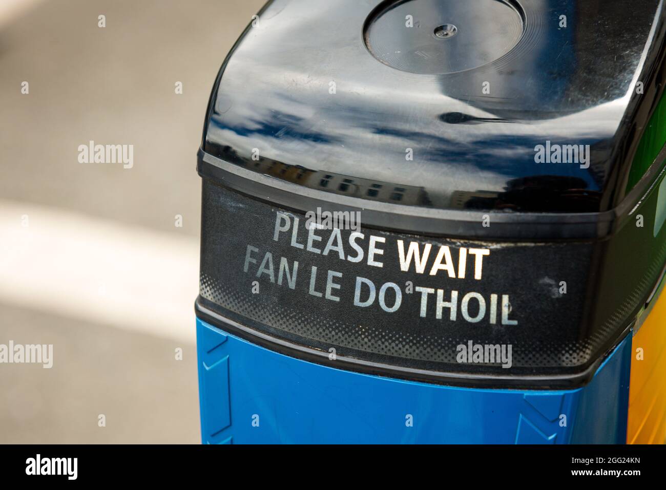 Please wait crosswalk button for pedestrians crossing, bilingual writing in English and Irish Gaelic, Ireland Stock Photo