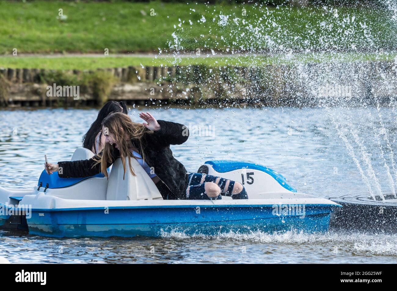 An excited teenage girl taking a selfie in a pedalo as she and her friend is getting soaked by the spray of an ornamental fountain on Trenance Boating Stock Photo