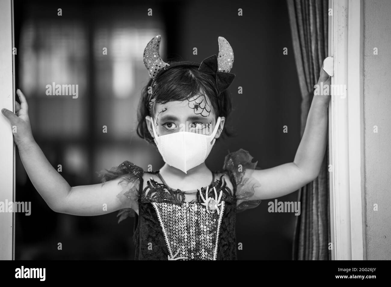 Grayscale shot of a Southeast Asian girl in a Halloween costume and makeup wearing a sanitary mask Stock Photo