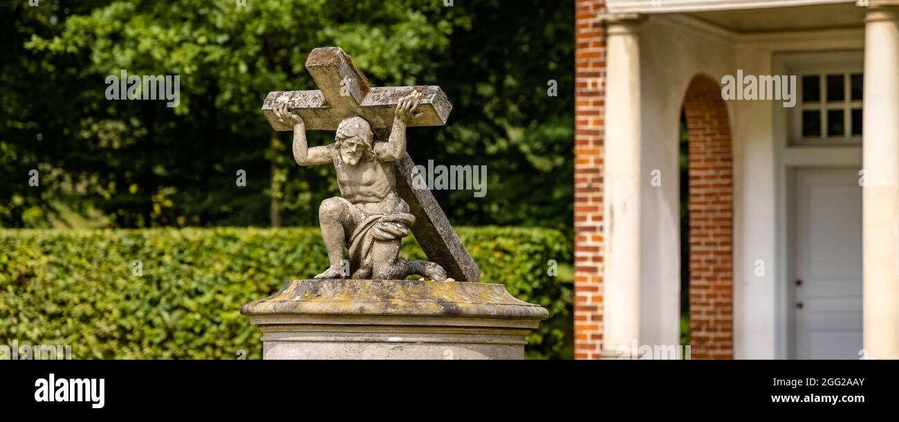 Sogel, Germany - August 25, 2021: Sculpture of Jesus carrying his cross in cloister garden at castle Clemenswerth in Sogel Lower Saxony in Germany Stock Photo