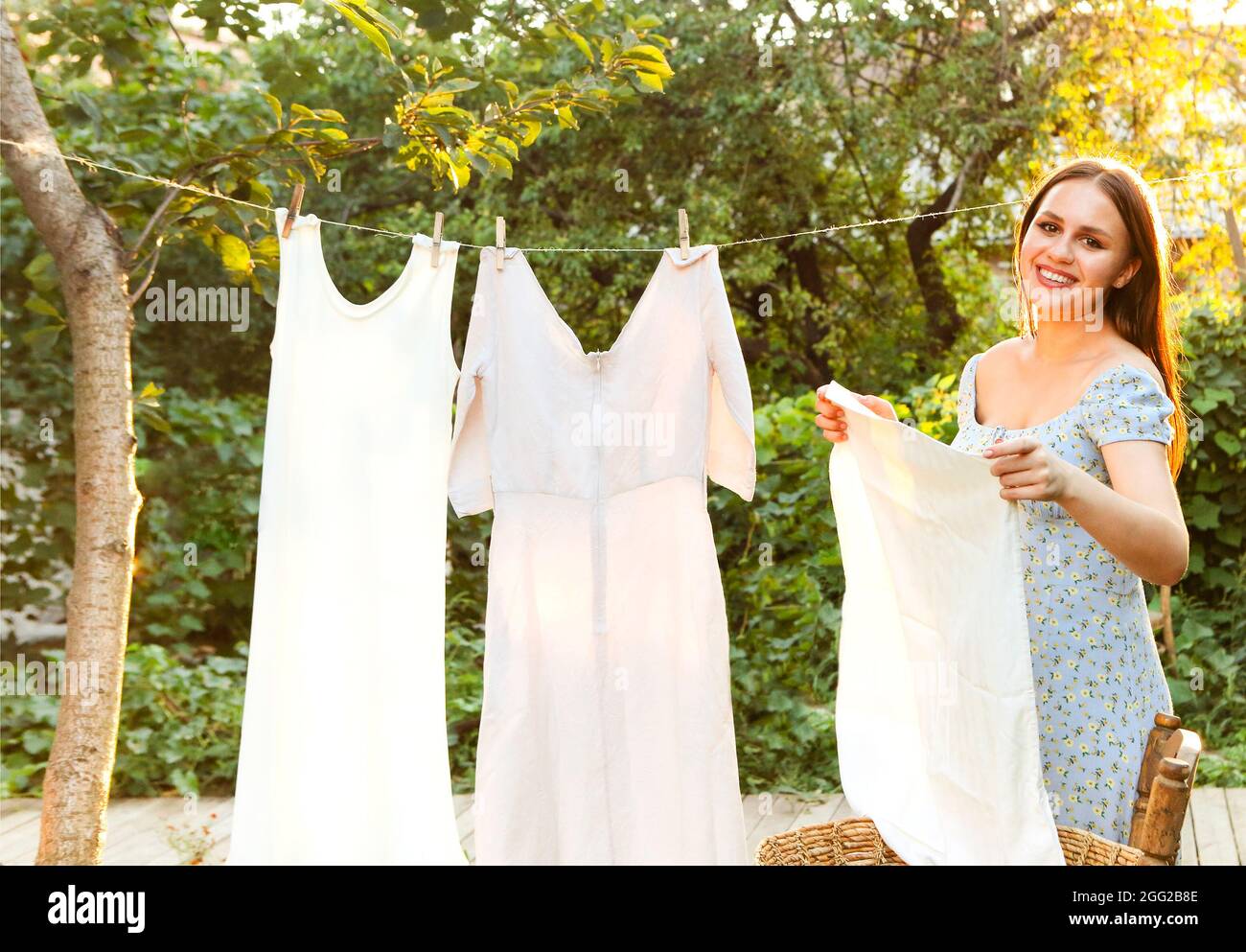 Young woman hanging laundry outdoors. Cute girl in dress washing white
