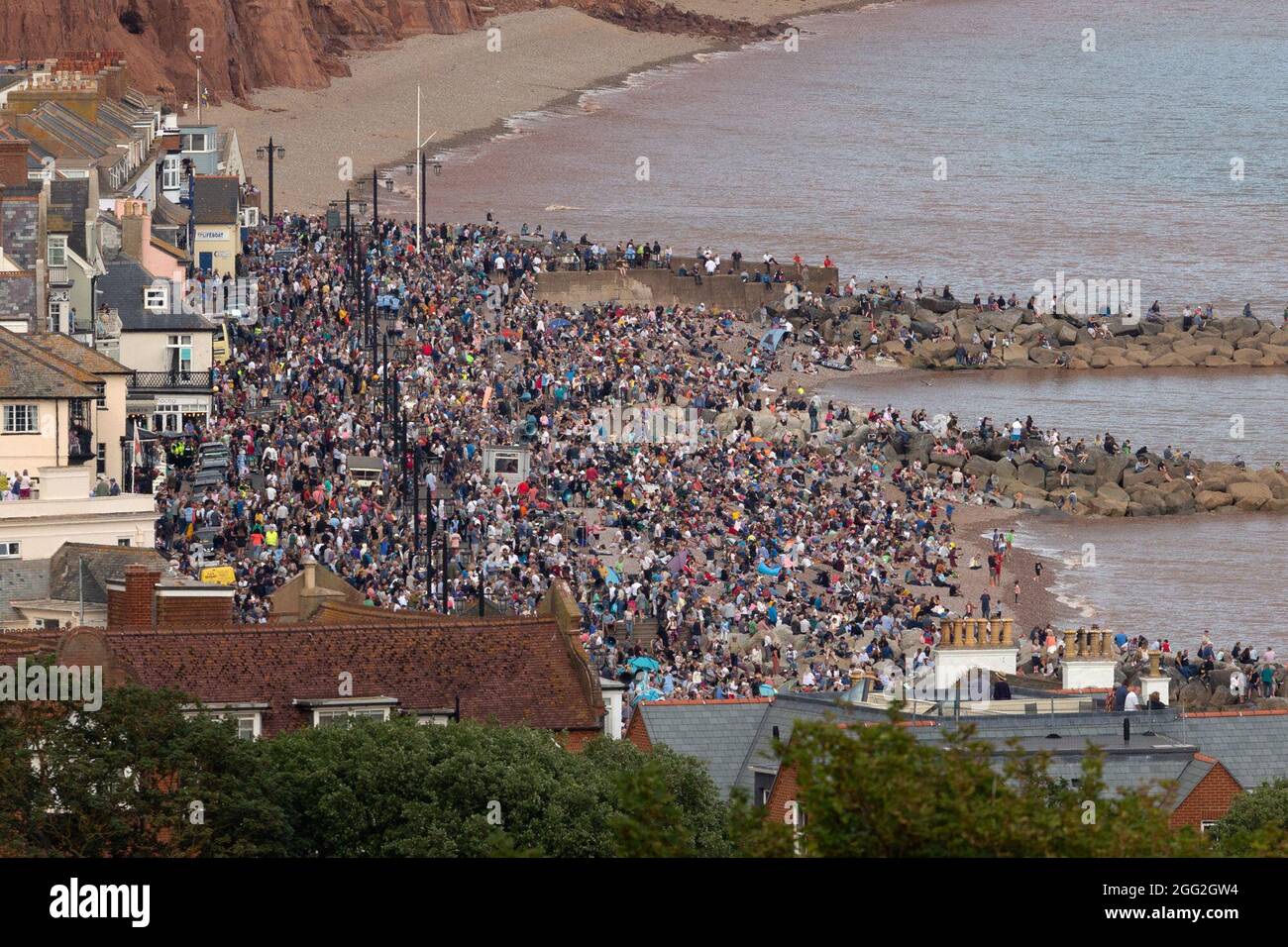 Sidmouth, Devon, UK. 27th Aug 2021.  Members of the public pack the seafront at Sidmouth in Devon to watch a spectacular display performed by the RAF Red Arrows. Credit: Ian Williams/Alamy Live News Stock Photo