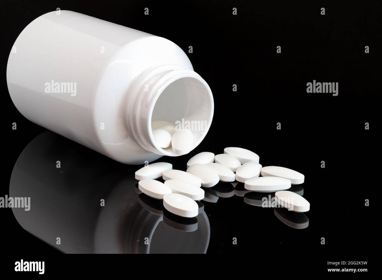 Opened bottle of medicine pills. Several pills are lying on background Stock Photo