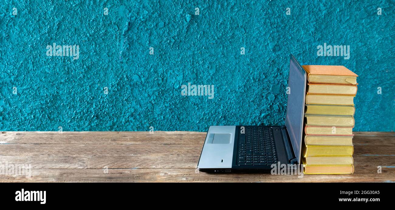 Stack of books and laptop computer,home office, homeschooling,reading,education, business concept. Free copy space,teal background, panoramic Stock Photo