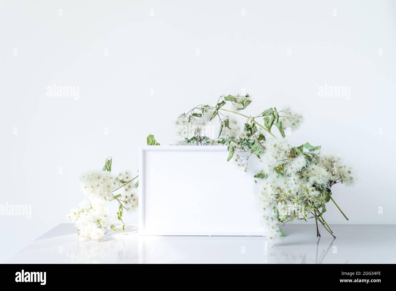 Empty white picture frame mockup. Elegant vintage branch wraps the frame. Minimalist and simple decoration. still life in daylight Stock Photo